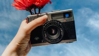 woman showing retro photo camera and holding blooming flower